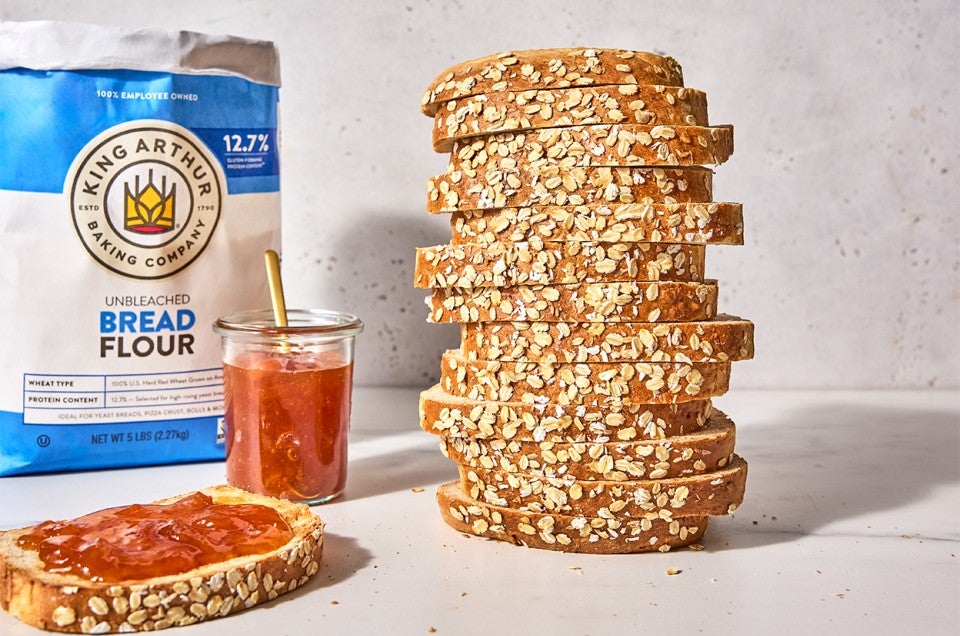 Back-of-the-Bag Oatmeal Bread towered high next to a slice with jam - select to zoom