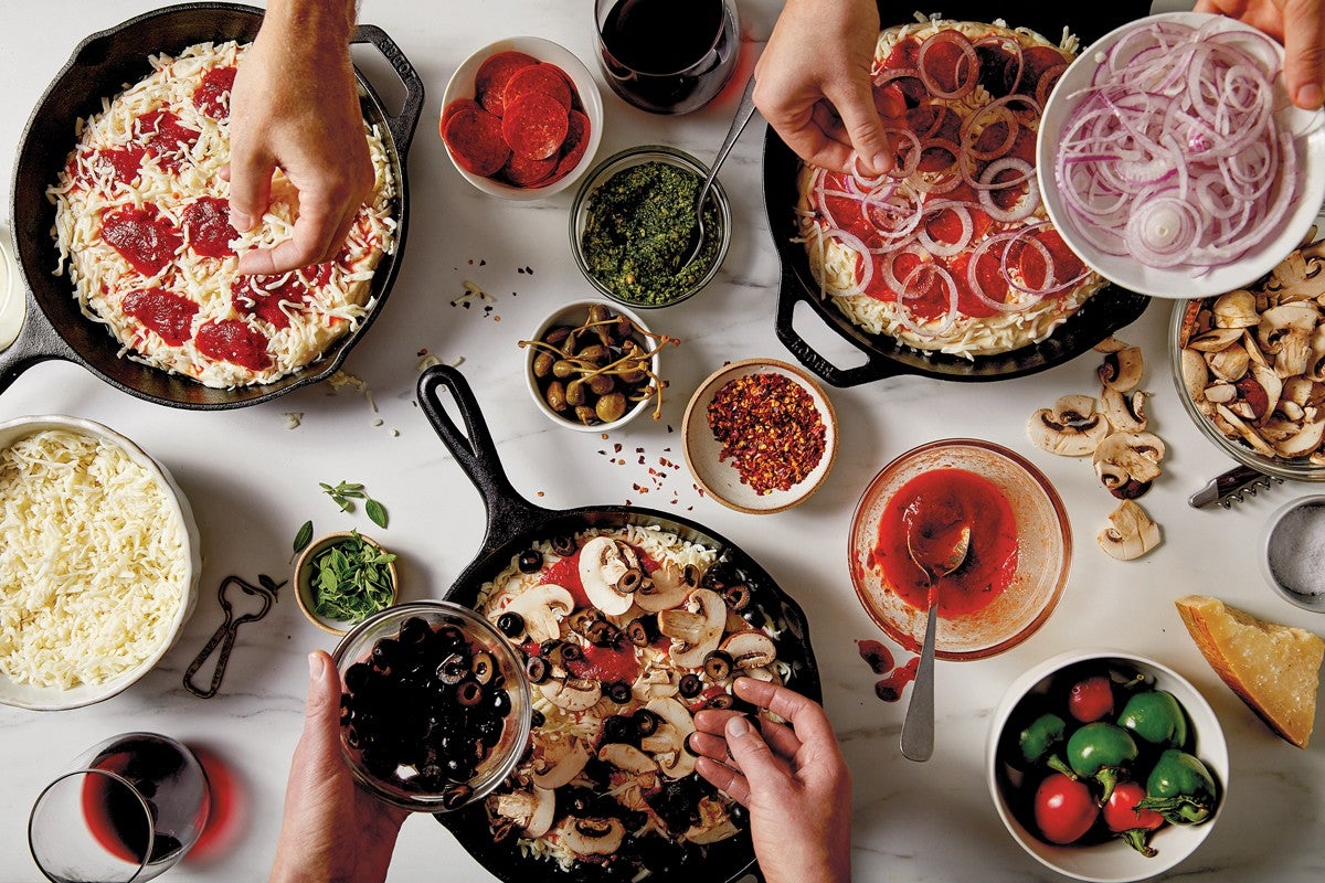 Bakers' hands adding toppings to three different pizzas