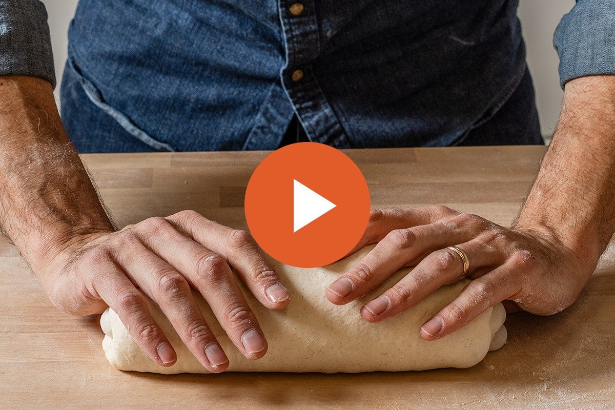 Hands shaping a batard, with a video play button graphic overlaid