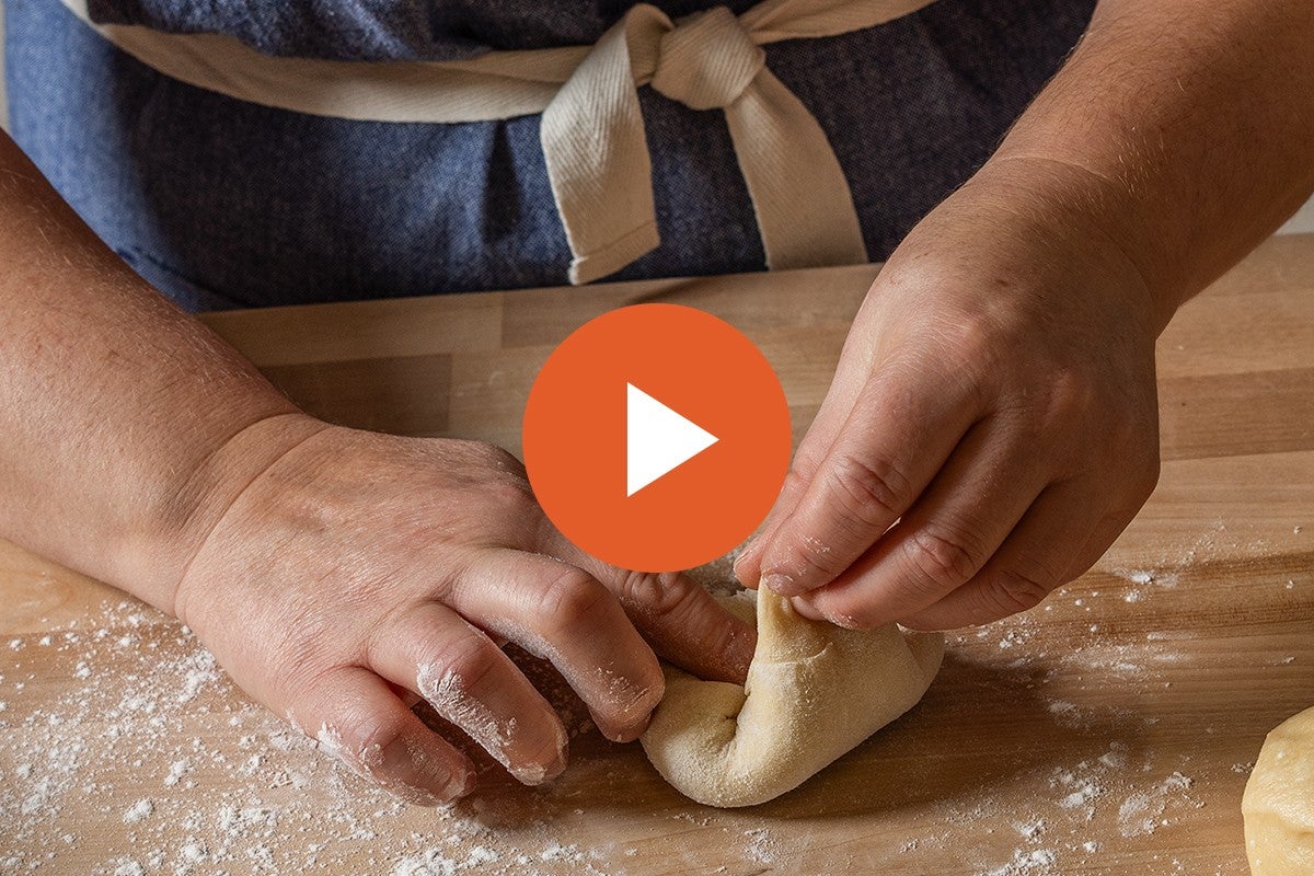 Hands shaping rolls, with a video play button graphic overlaid