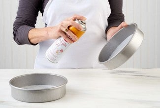 Round cake pans, lined with parchment, being sprayed with nonstick vegetable oil spray.