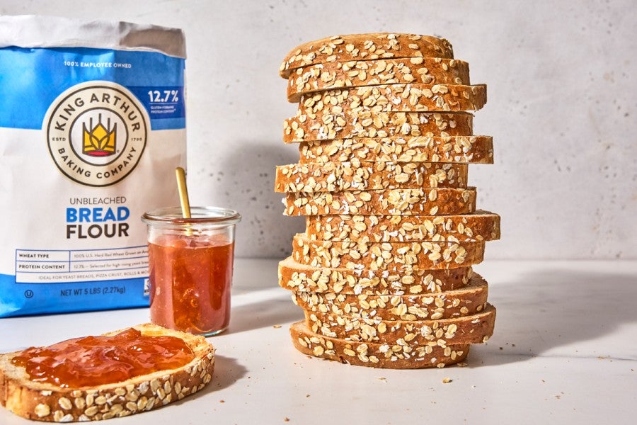 Bag of bread flour behind a sliced loaf of oatmeal sandwich bread